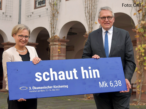 Das Präsidium des Ökumenischen Kirchentags, Bettina Limperg und Thomas Sternberg halten ein Schild hoch, auf dem das Leitwort des Ökumenischen Kirchentags steht: Schaut hin!