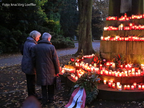 Zwei Frauen stehen vor einem Denkmal mit Kerzen.