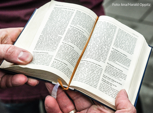 Ein Mann hält eine aufgeschlagene Bibel in der Hand.