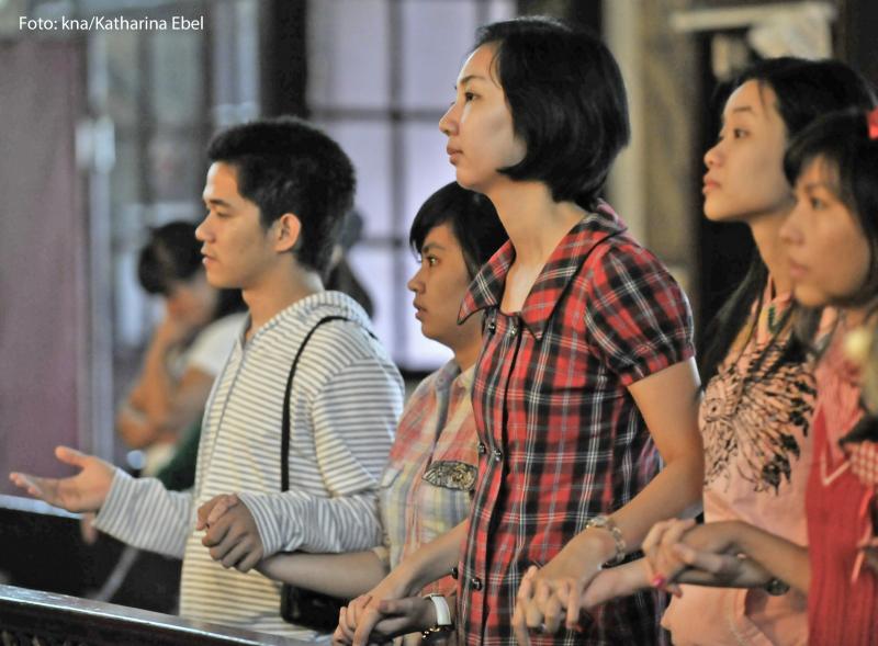 Chinesische Christen stehen in einer Kirchenbank und beten. 