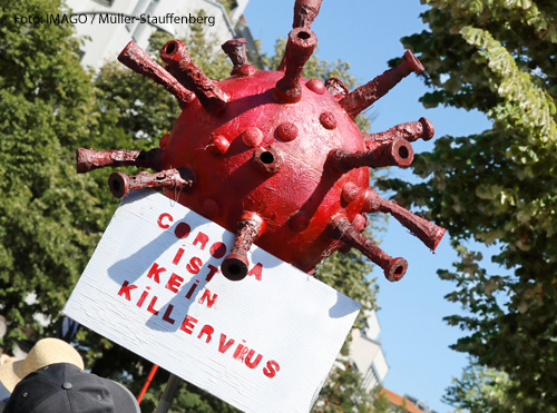 Ein Mann hält bei einer Demonstration ein Plakat hoch. Darauf steht "Corona ist kein Killervirus". 