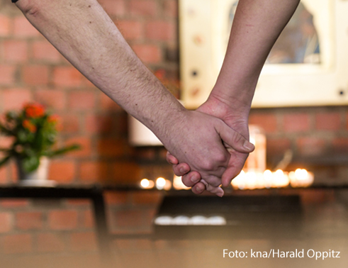 Zwei Männer halten sich an der Hand vor einem Altar. 