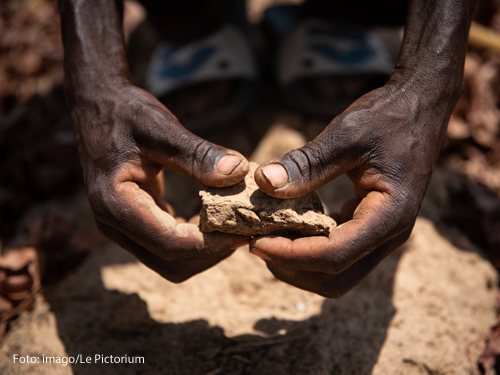 Ein Mann in Afrika zeigt, wie trocken sein Acker durch die Dürre geworden ist. 