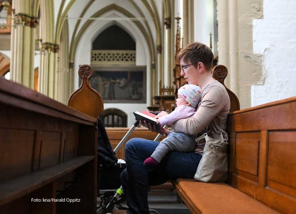 Eine Mutter sitzt mit ihrem Kind in einer Kirchenbank. 