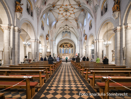 In einer Kirche stehen vereinzelt ein paar Gottesdienstteilnehmer. Viele Kirchenbänke sind mit Absperrband verschlossen. 