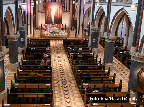 Blick von oben auf halbleere Kirchenbänke mit wenigen Gottesdienstteilnehmern während eines Gottesdienstes 