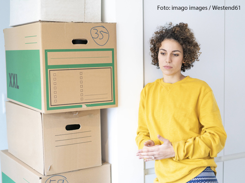 Eine Frau steht neben gepackten Umzugskartons. Sie sieht nachdenklich aus. 