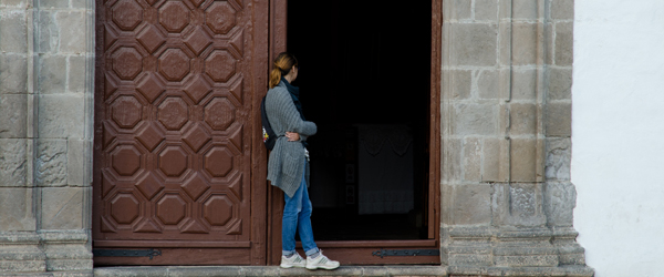 Frau steht vor Kirche und schaut hinein. Foto: Adobe Stock