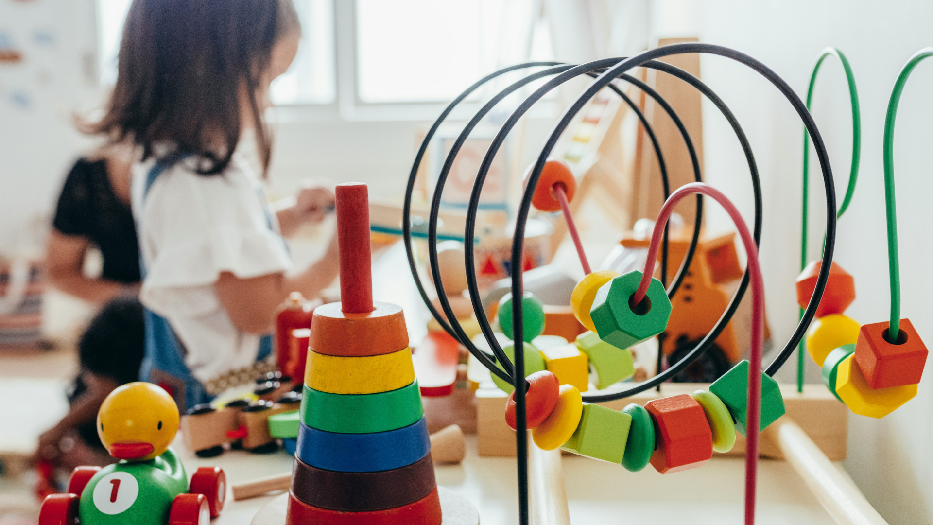 Im Vordergrund Kinderspielzeug, im Hintergrund ein Kind beim spielen
