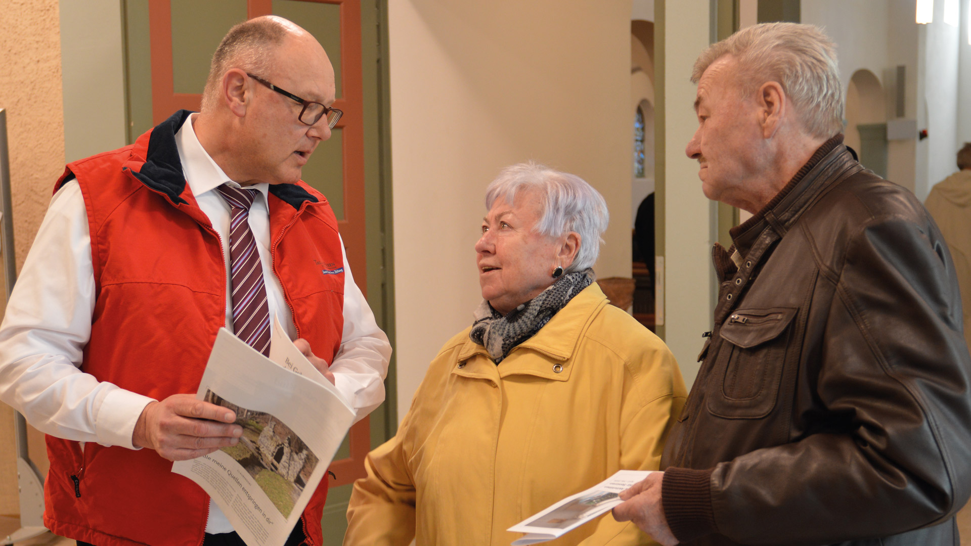 Willi Krug im Gespräch mit einem Ehepaar vor einer Kirche