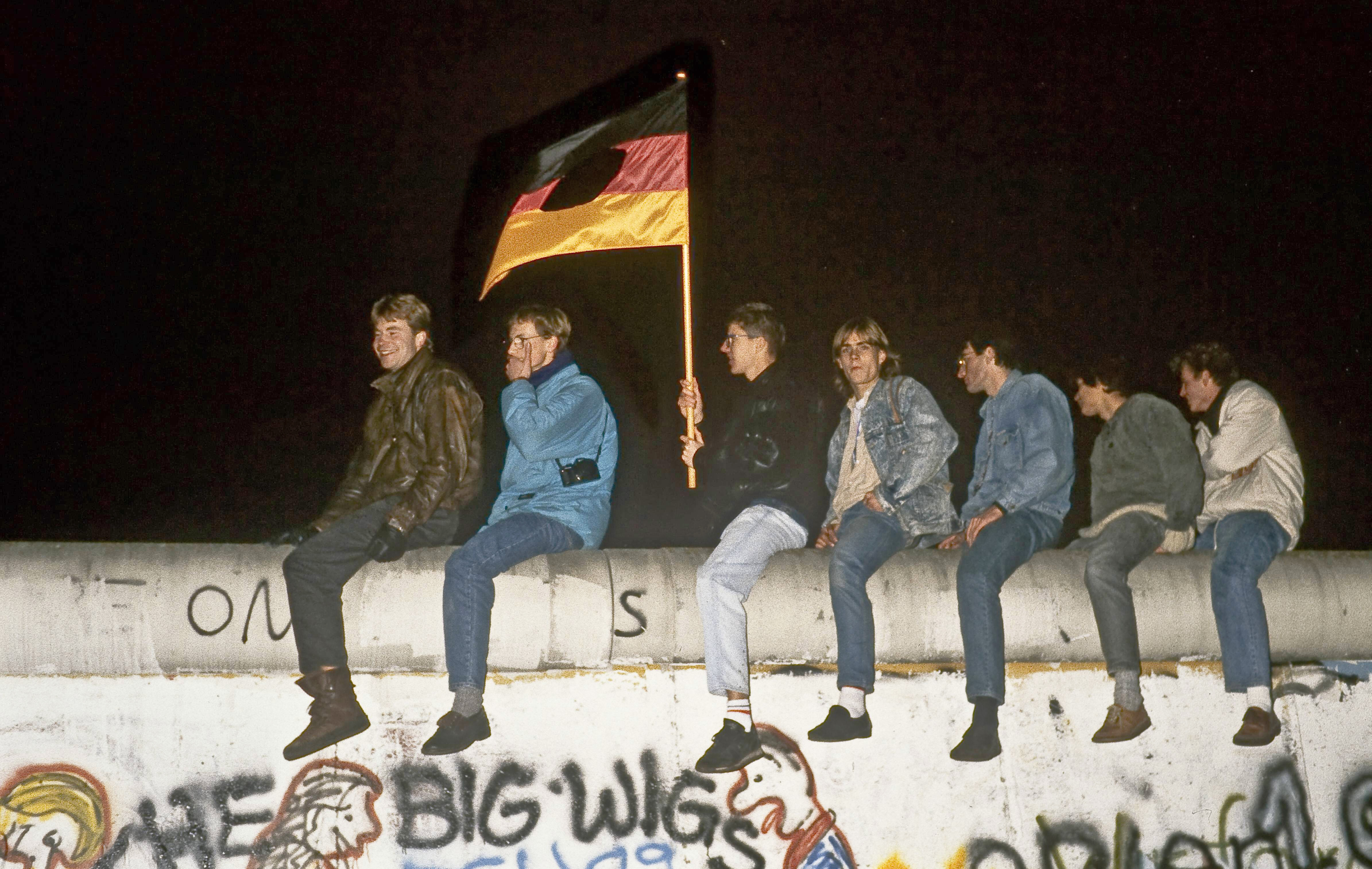 Menschen sitzen mit einer Deutschlandflagge auf der Berliner Mauer