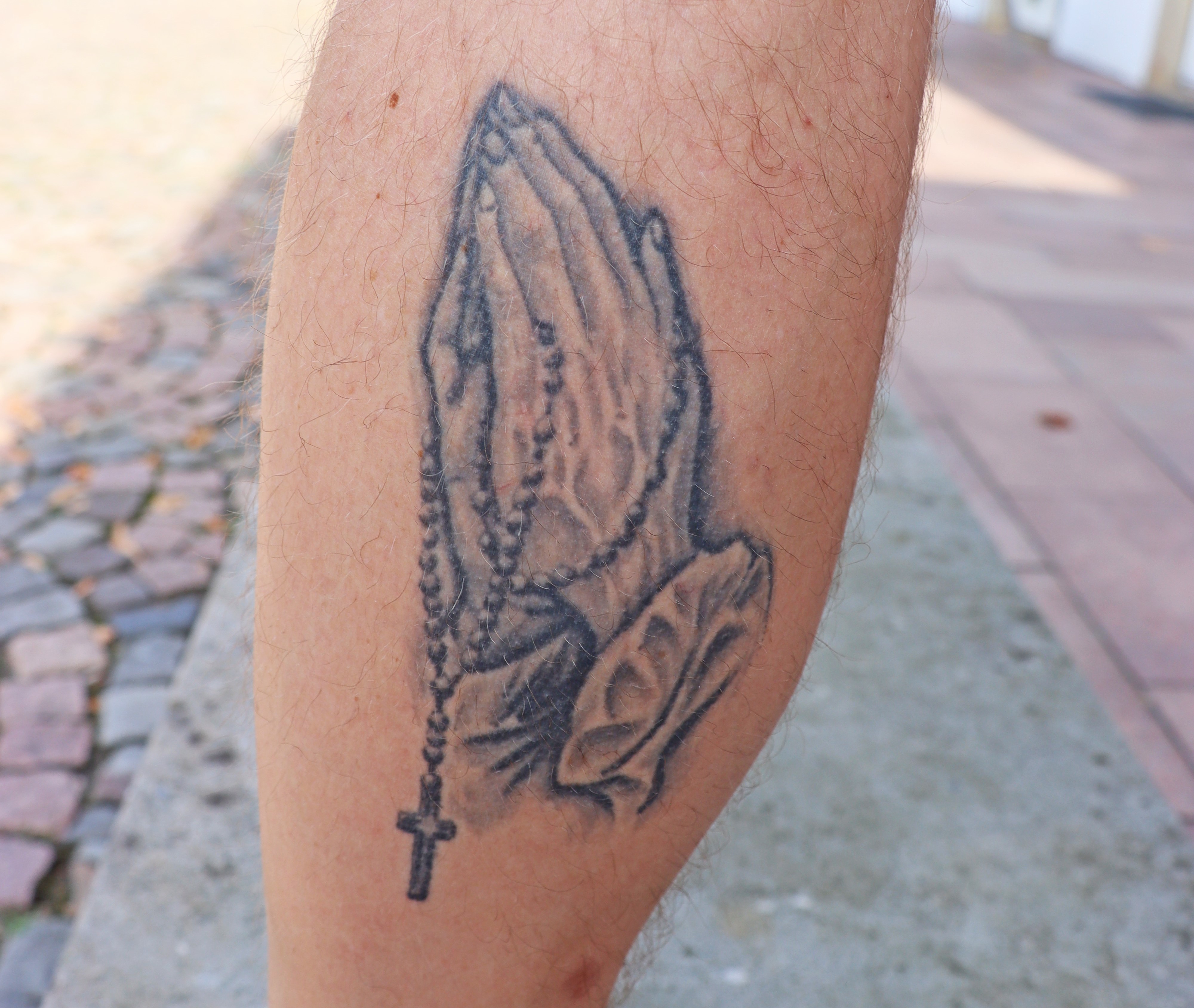 Nahaufnahme von einer Wade, darauf ein Tattoo von betenden Händen