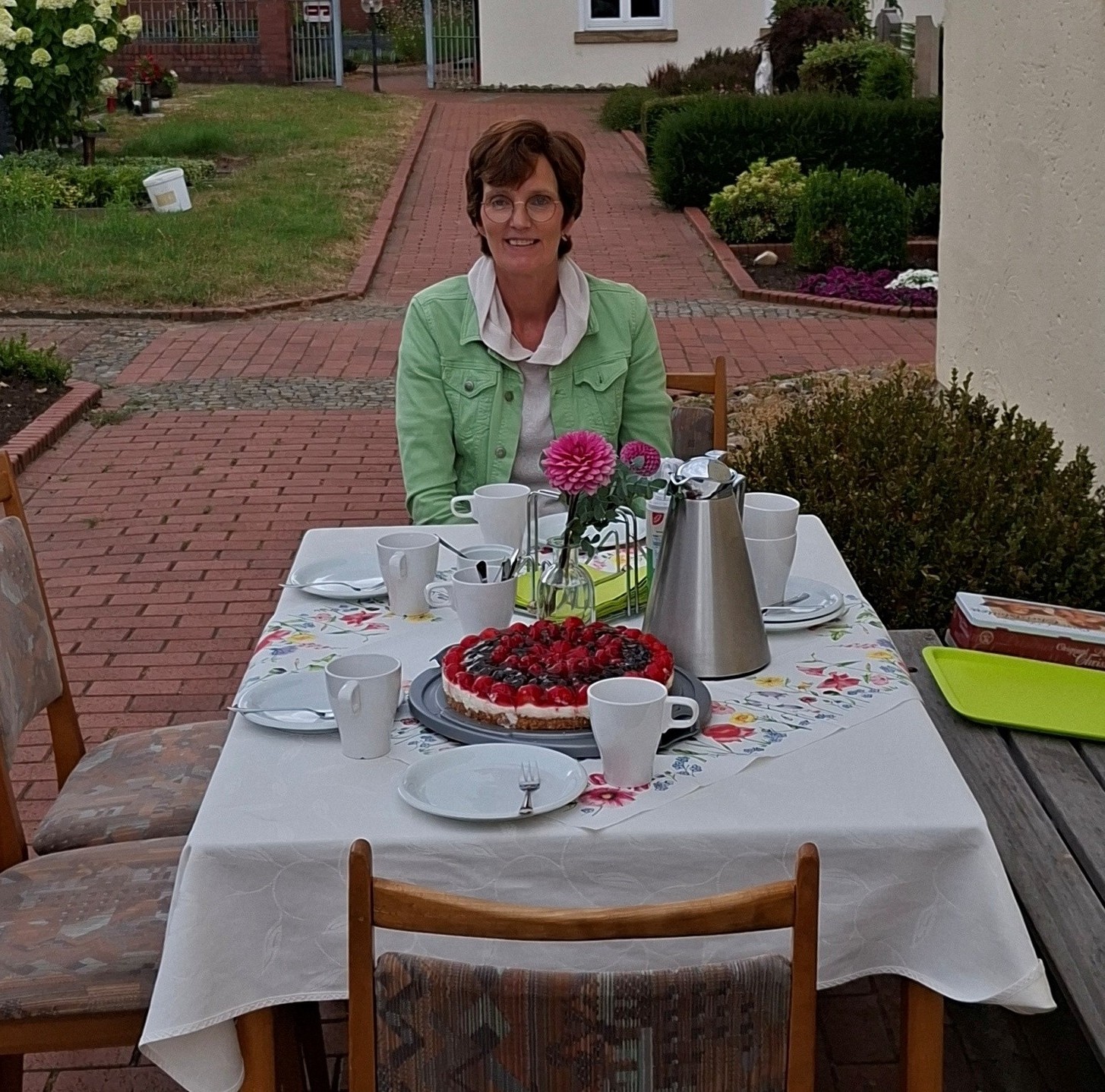 Eine Frau sitzt draußen an einem gedeckten Kaffeetisch.