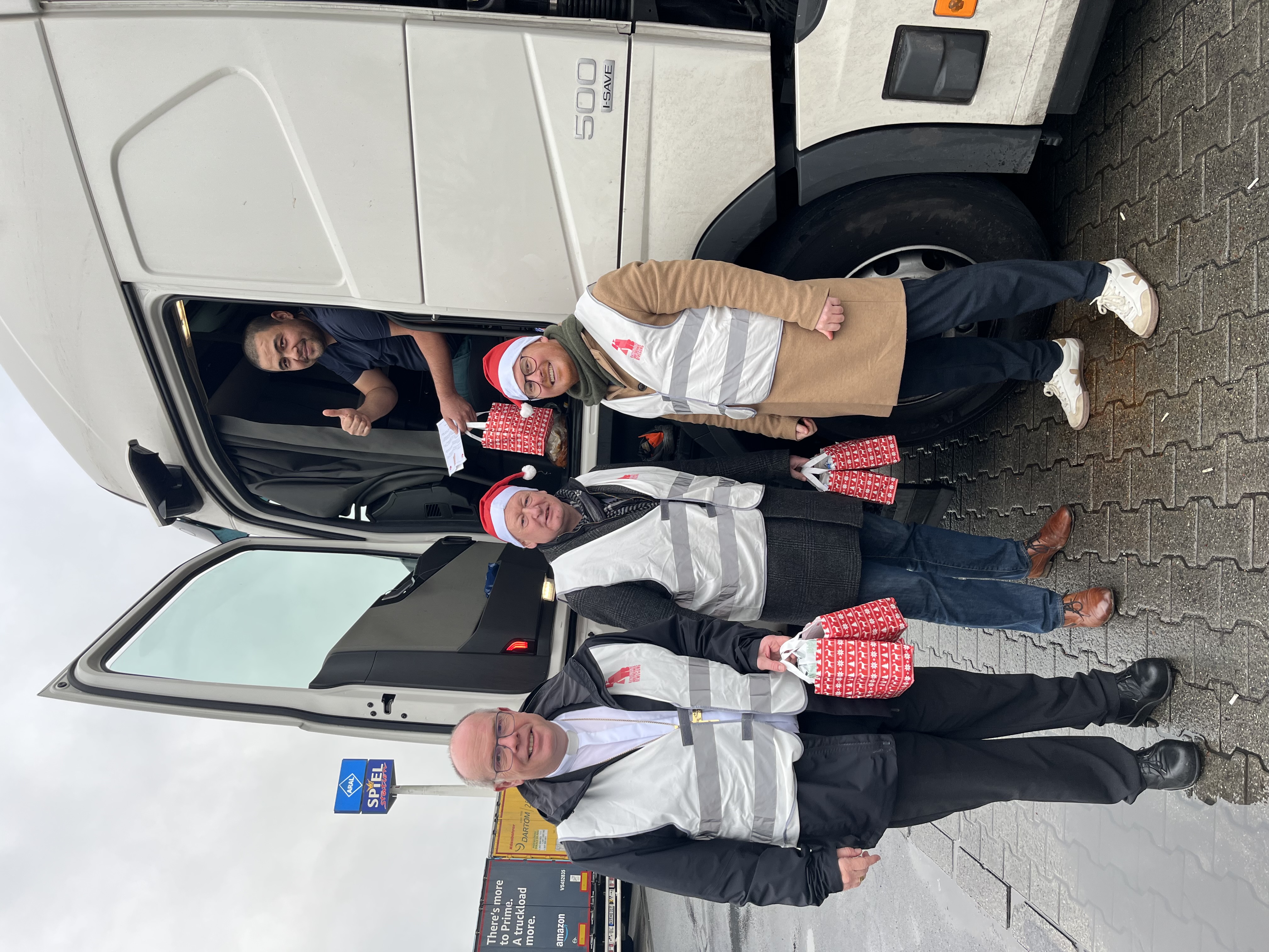 Drei Männer stehen vor einem Lkw. Aus der geöffneten Tür blickt der Fahrer in die Kamera