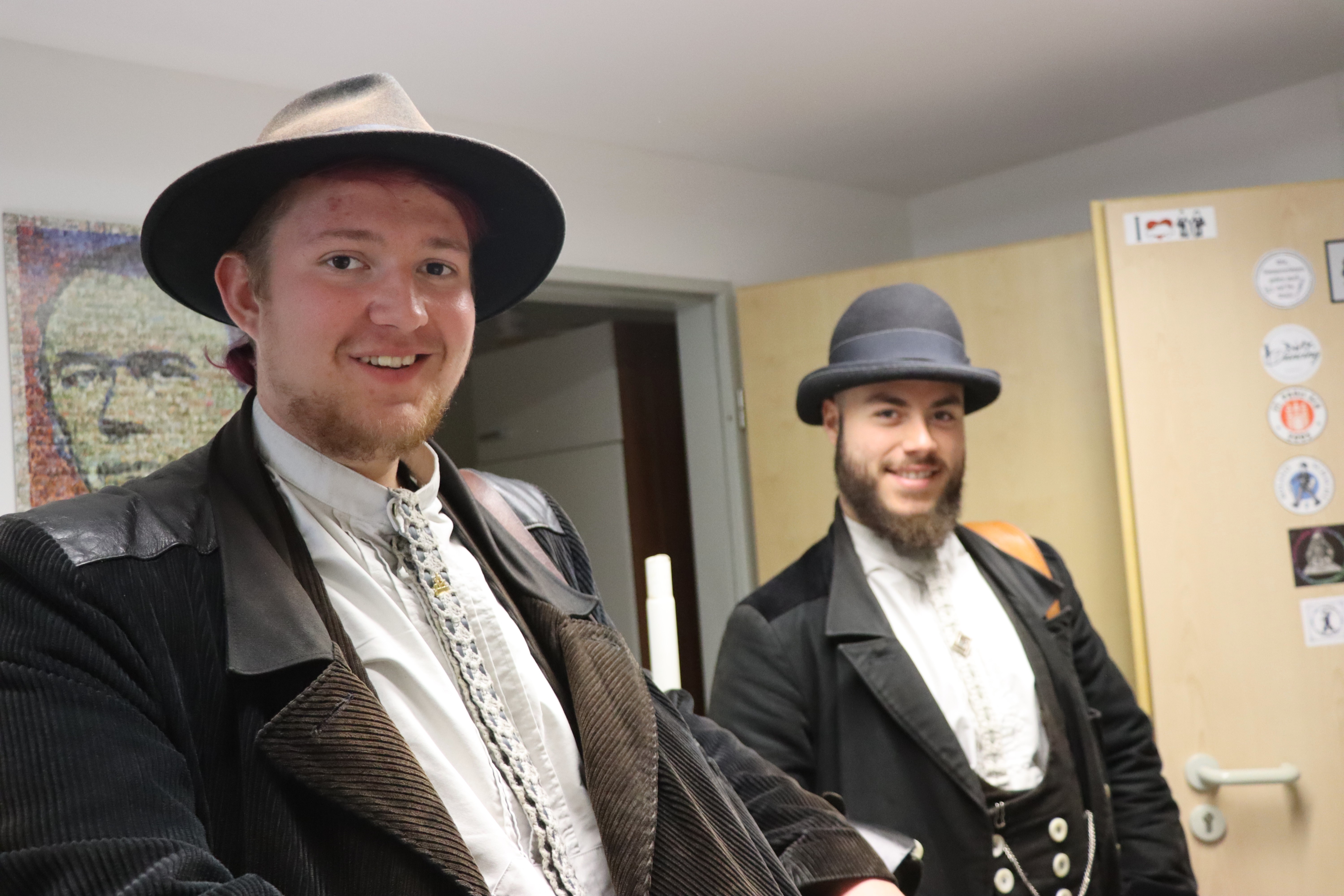 Zwei junge Männer stehen in einem Zimmer. Es ist die Unterkunft mit Stockbetten im Osnabrücker Kolpinghaus. Beide schauen in die Kamera und lächeln. Im Hintergrund erkennt man ein Bild des Pfarrers Adolph Kolping, dem Gründer der Kolpingsfamilien.