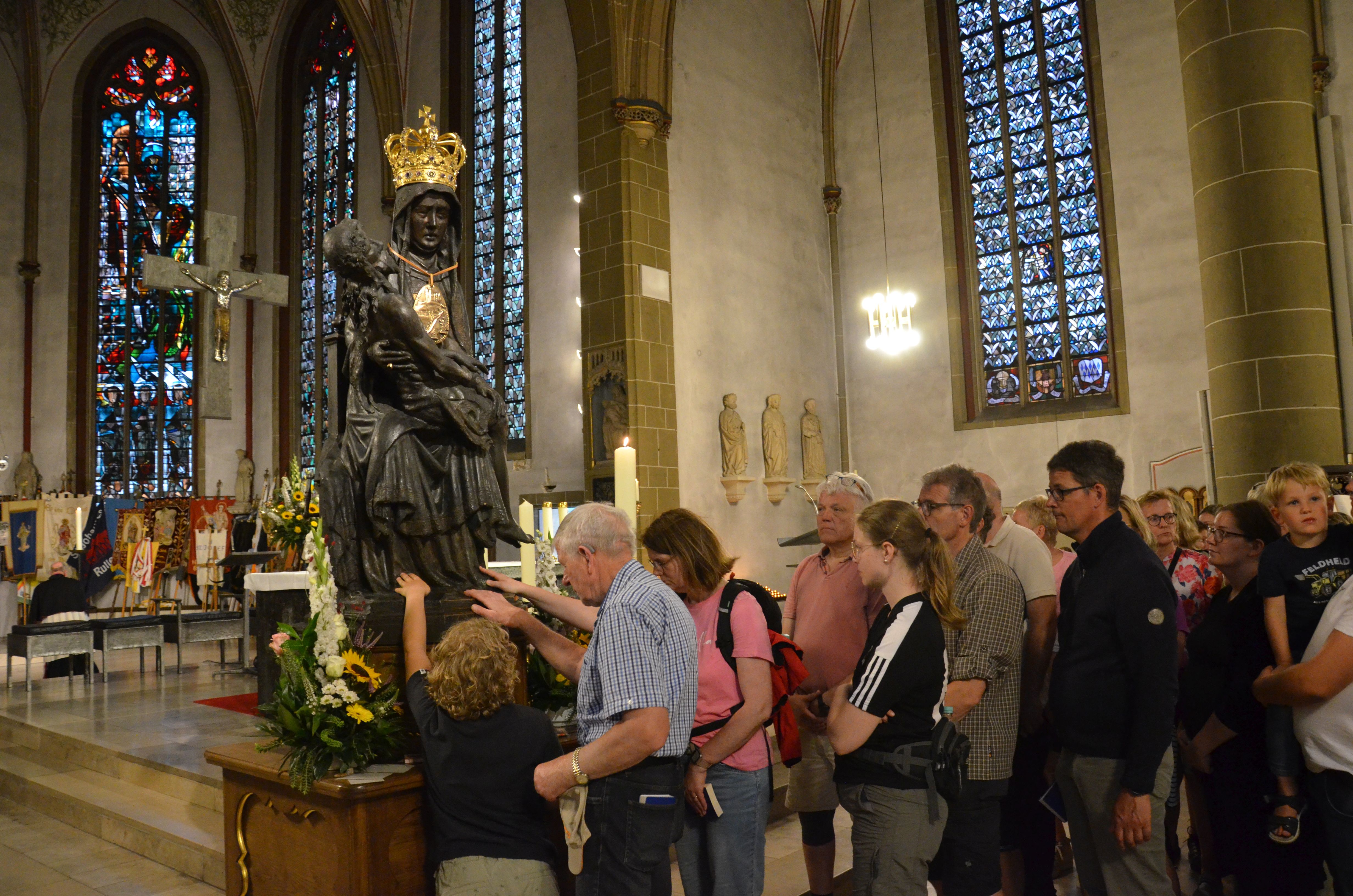 Junge und ältere Menschen stehen in einer Warteschlange, um vor der Muttergottesstatue zu beten