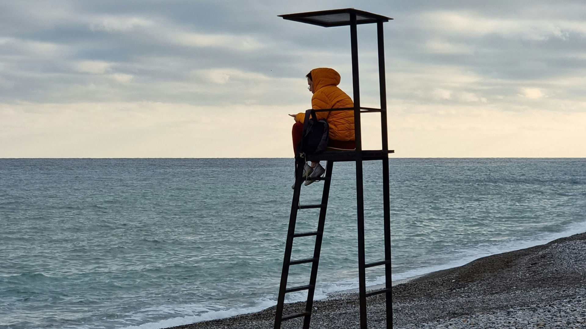 Ein Mensch sitzt auf einem Hochsitz vor dem Meer