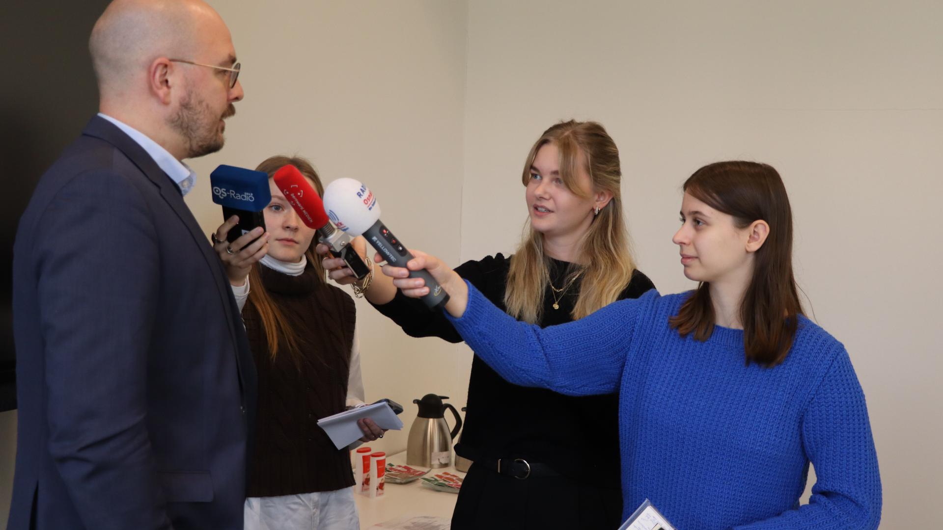 Drei junge Frauen befragen einen Mann und haben Hörfunkmikrofone in der Hand