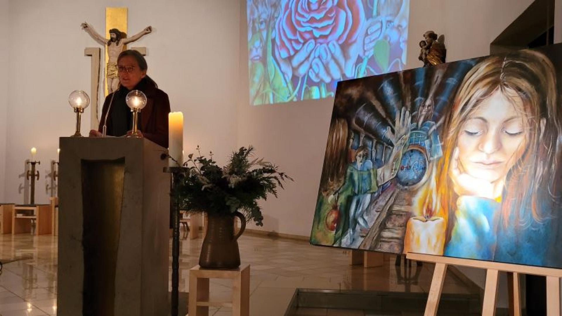 Eine Frau steht in einer Kirche am Ambo, neben ihr ein Kunstwerk.