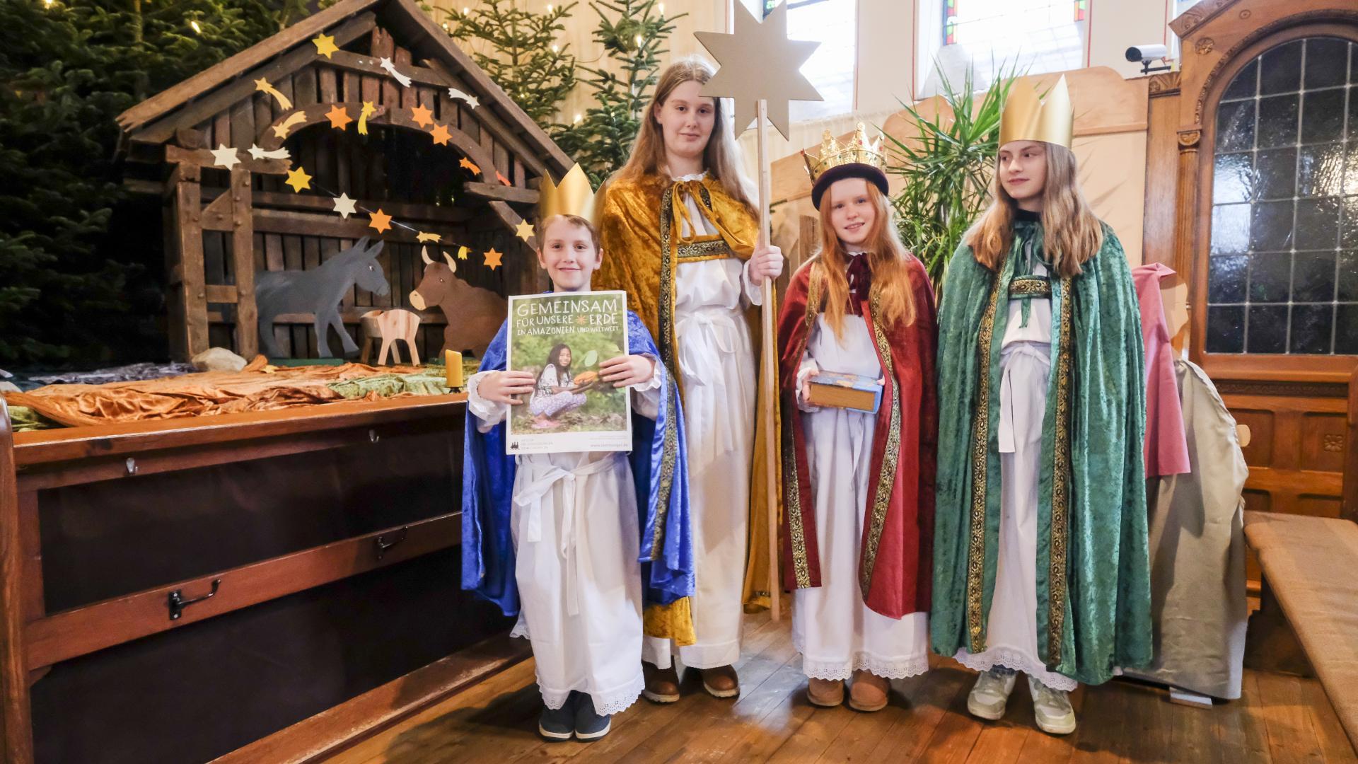 Vier als Sternsinger verkleidete Kinder stehen vor einer Weihnachtskrippe