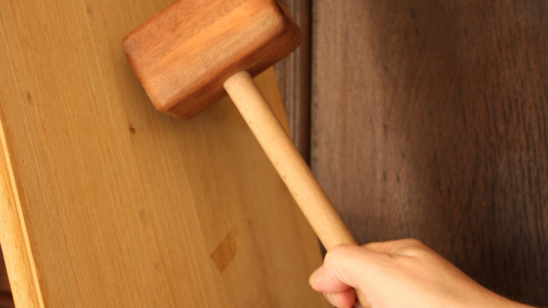 Ein Holzhammer wird von einer Hand auf ein Brett gehauen