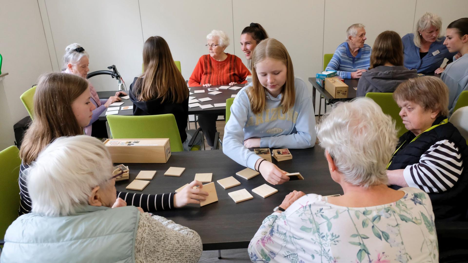 Mehrere Seniorinnen sitzen mit einer jungen Schülerin am Tisch und spielen Memory