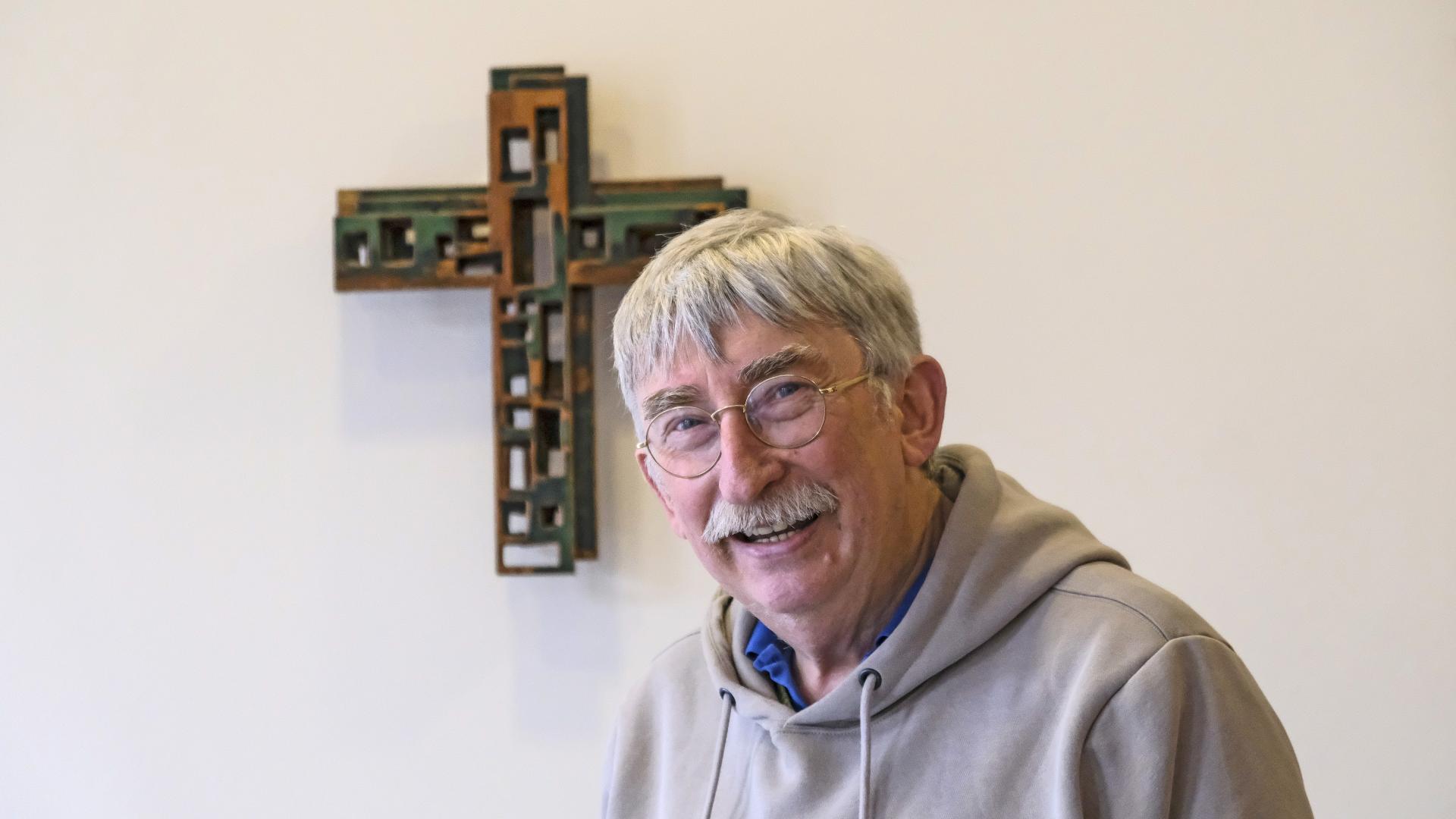 Porträtfoto eines Mannes, der vor einem Kreuz sitzt