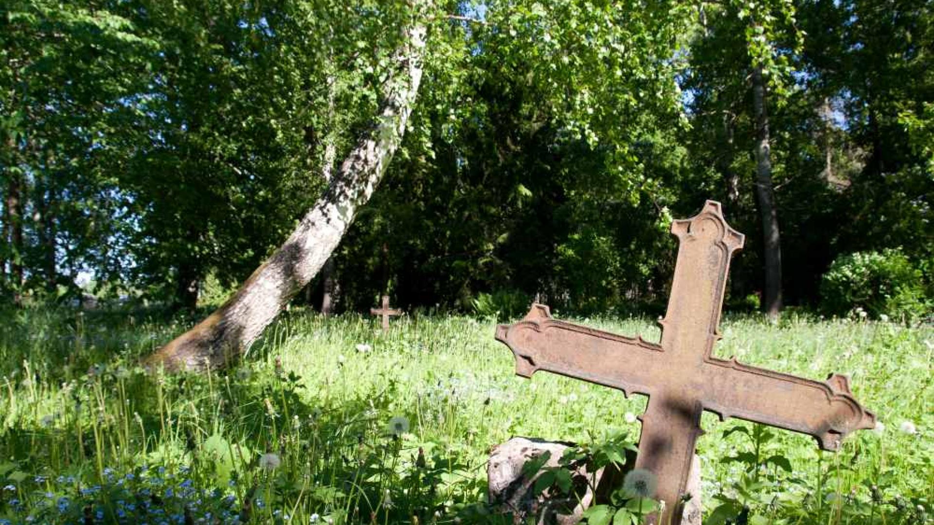 Verwittertes Grabkreuz auf einer Wiese, die mal ein Friedhof war.