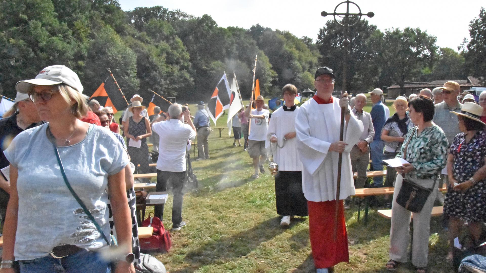 Menschen mit Kreuz und Fahnen auf einer Wiese.