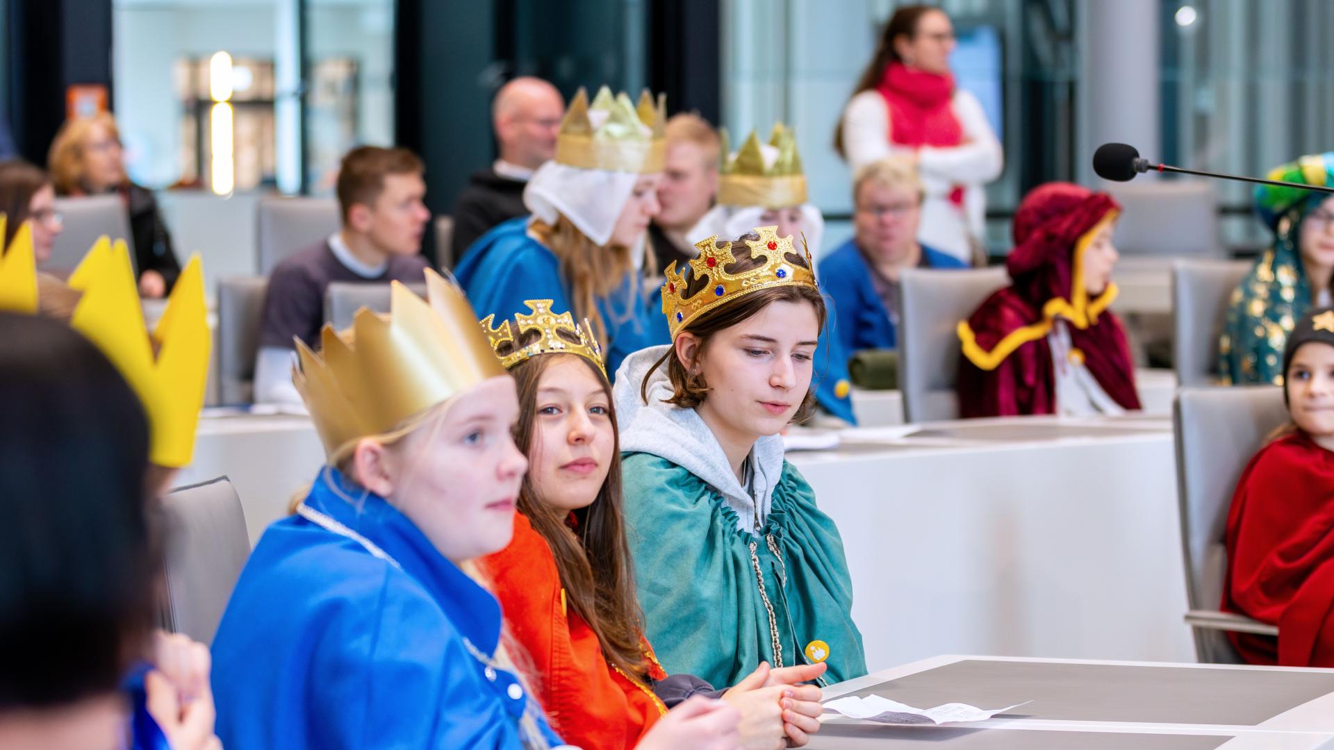 Mehrere als Sternsinger verkleidete Kinder sitzen an Tischen in einem Plenarsaal