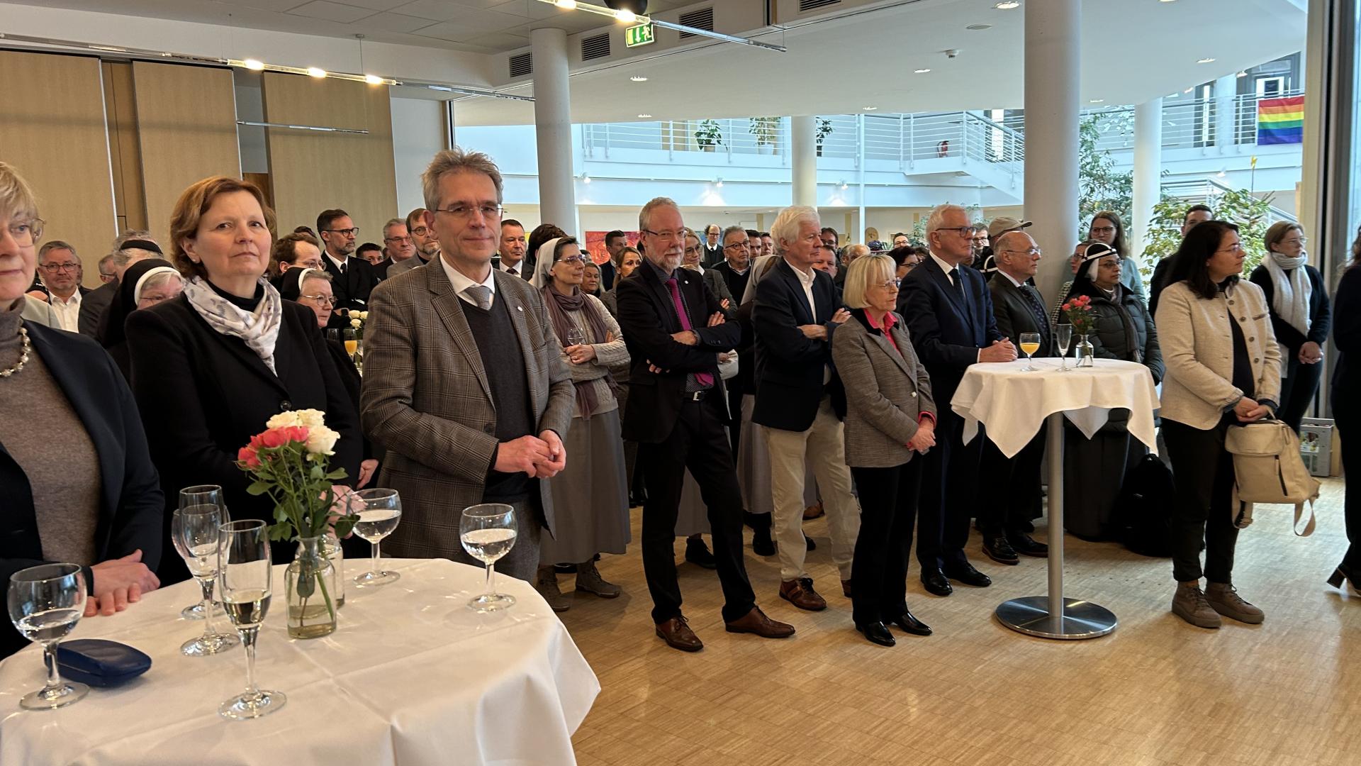 Eine große Gruppe Menschen steht in einem Raum, im Vordergrund zwei Stehtische