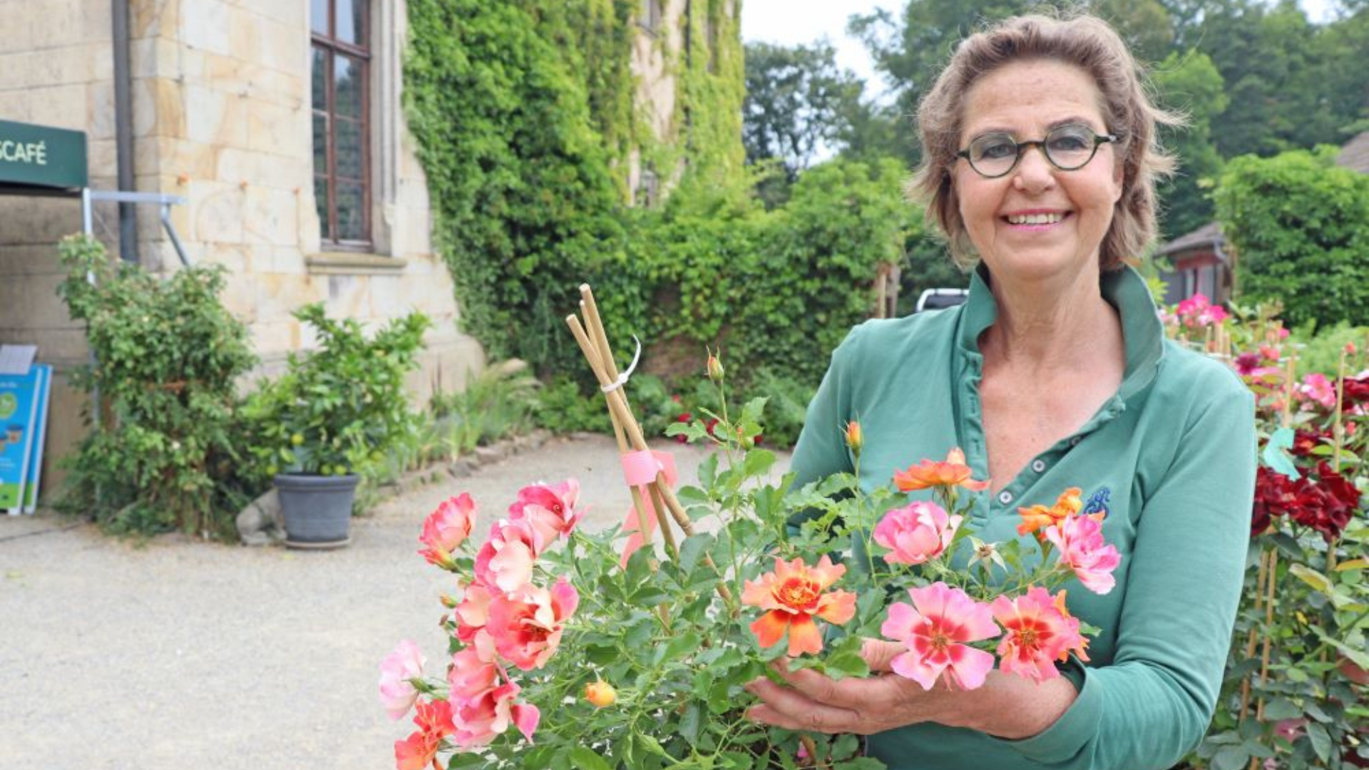 Frau zeigt einen Topf mit blühenden Pflanzen in die Kamera