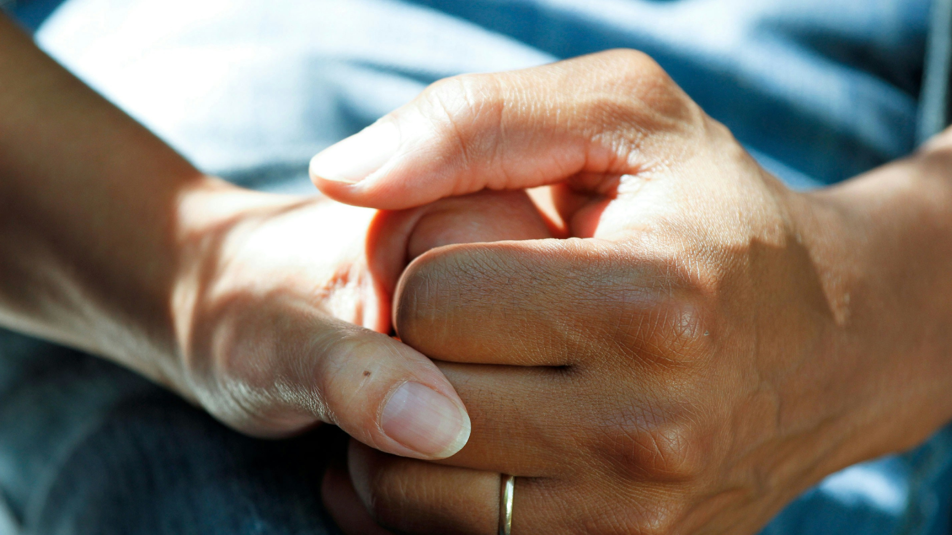 Eine Hand wird von einer anderen auf einem Schoß gehalten