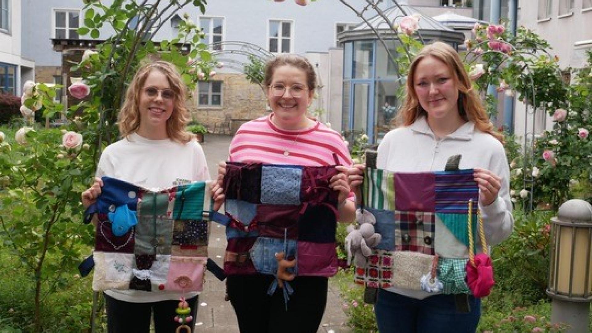 Drei Frauen mit kleinen Deckchen in der Hand