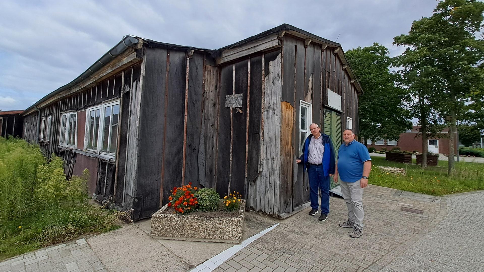 Zwei Männer stehen vor einer Holzbaracke