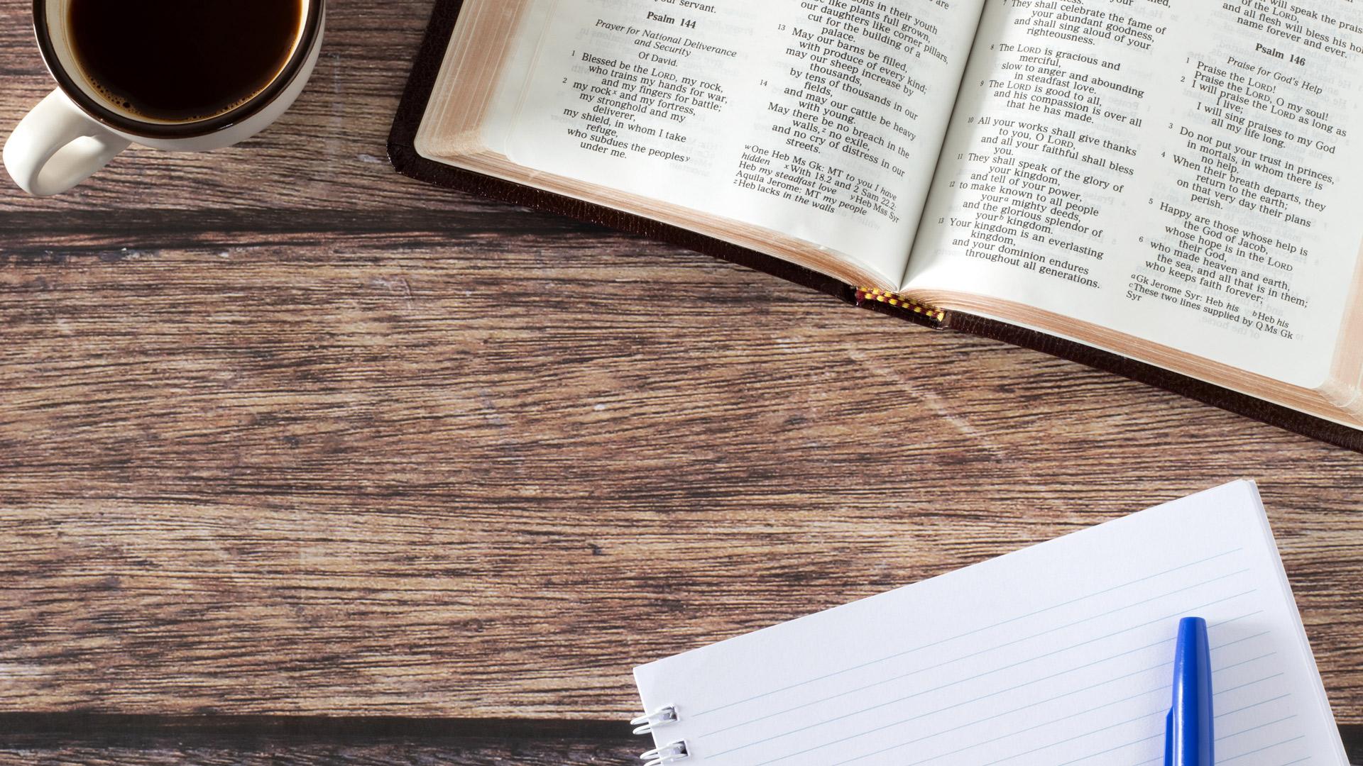aufgeschlagene Bibel, eine Kaffeetasse und ein Schreibblock auf einem Tisch