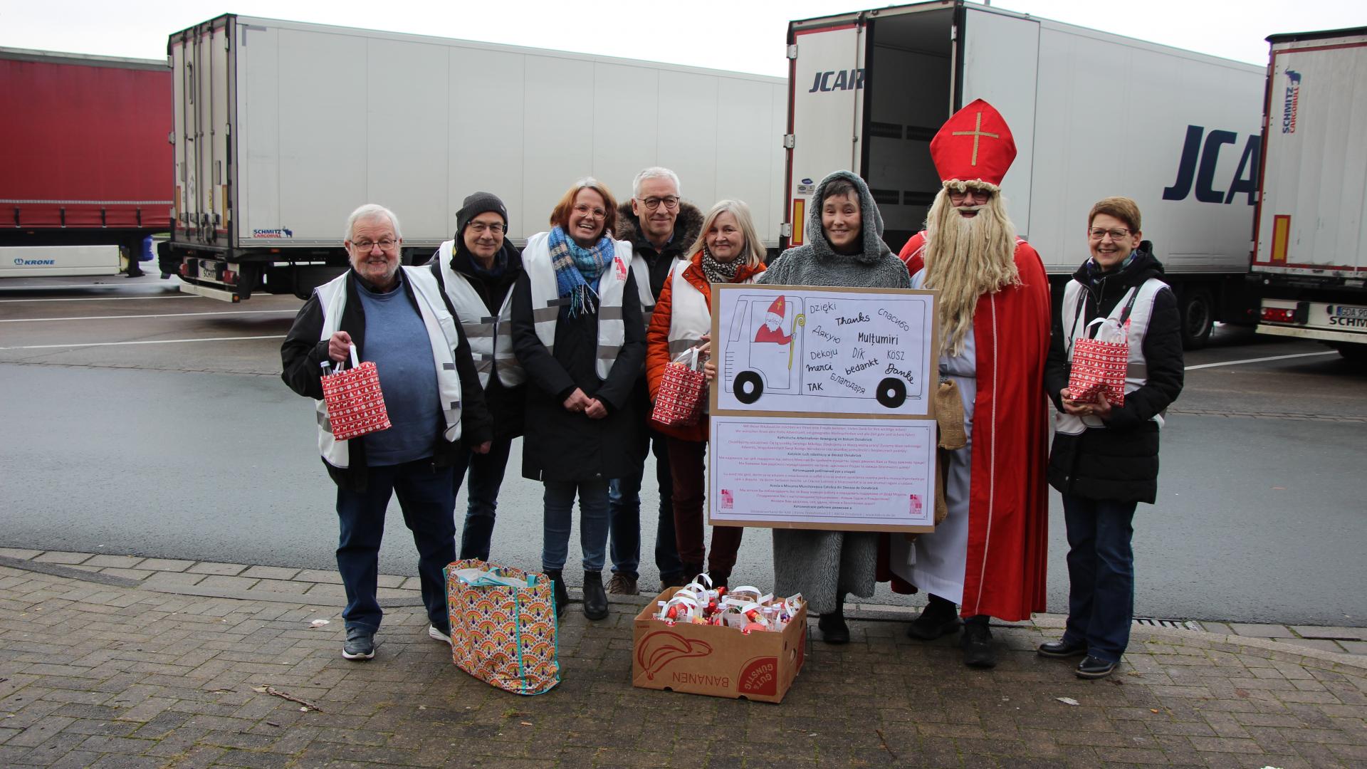 Eine Gruppe von Menschen steht auf einem Rastplatz vor einem Lkw. Ein Mann ist als Nikolaus verkleidet
