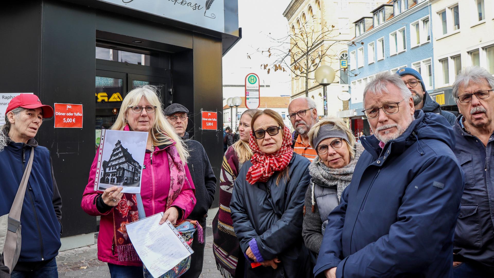Eine Gruppe von Menschen ist bei einer Stadtführung, eine Frau hält eine Fotografie hoch