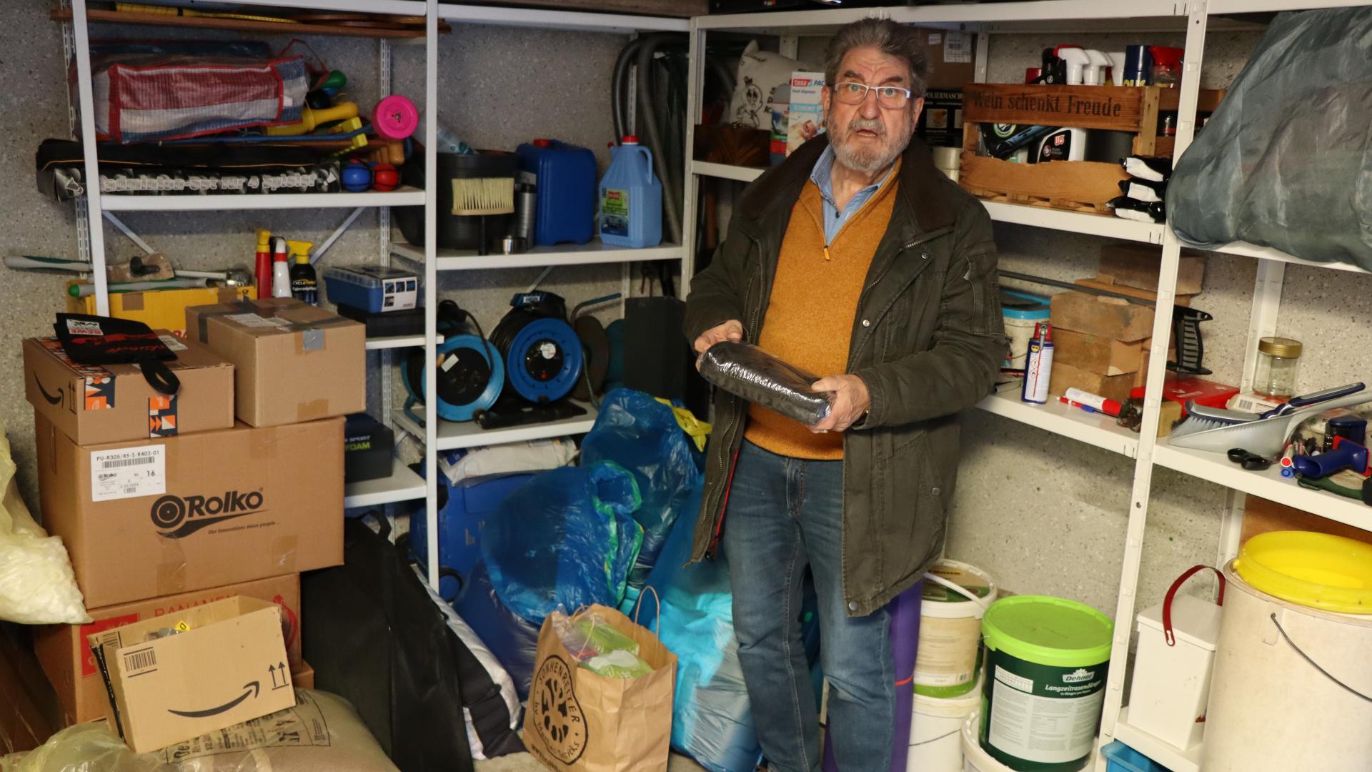 Ein Mann steht in einer Garage, hinter ihm Regale gefüllt mit Gegenständen