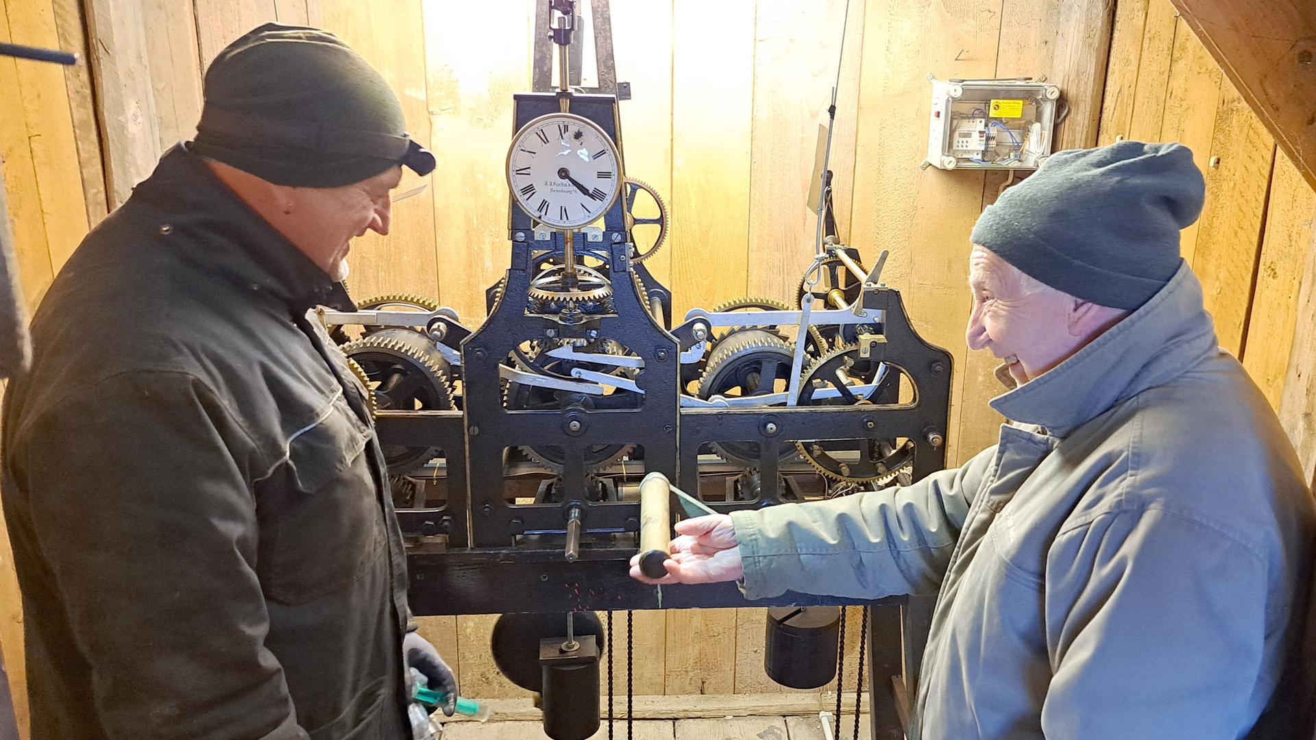 zwei Männer stehen vor einem mechanischen Uhrwerk in einem Kirchenturm