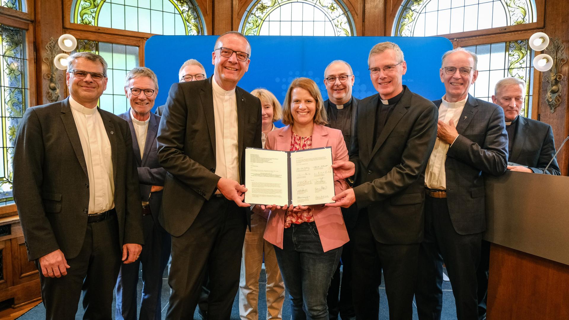 Eine größere Menschengruppe hält ein Schriftstück in die Kamera