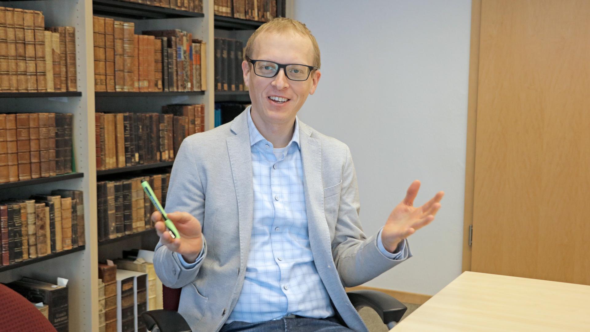 Ein Mann lächelt in die Kamera und gestikuliert mit den Händen.