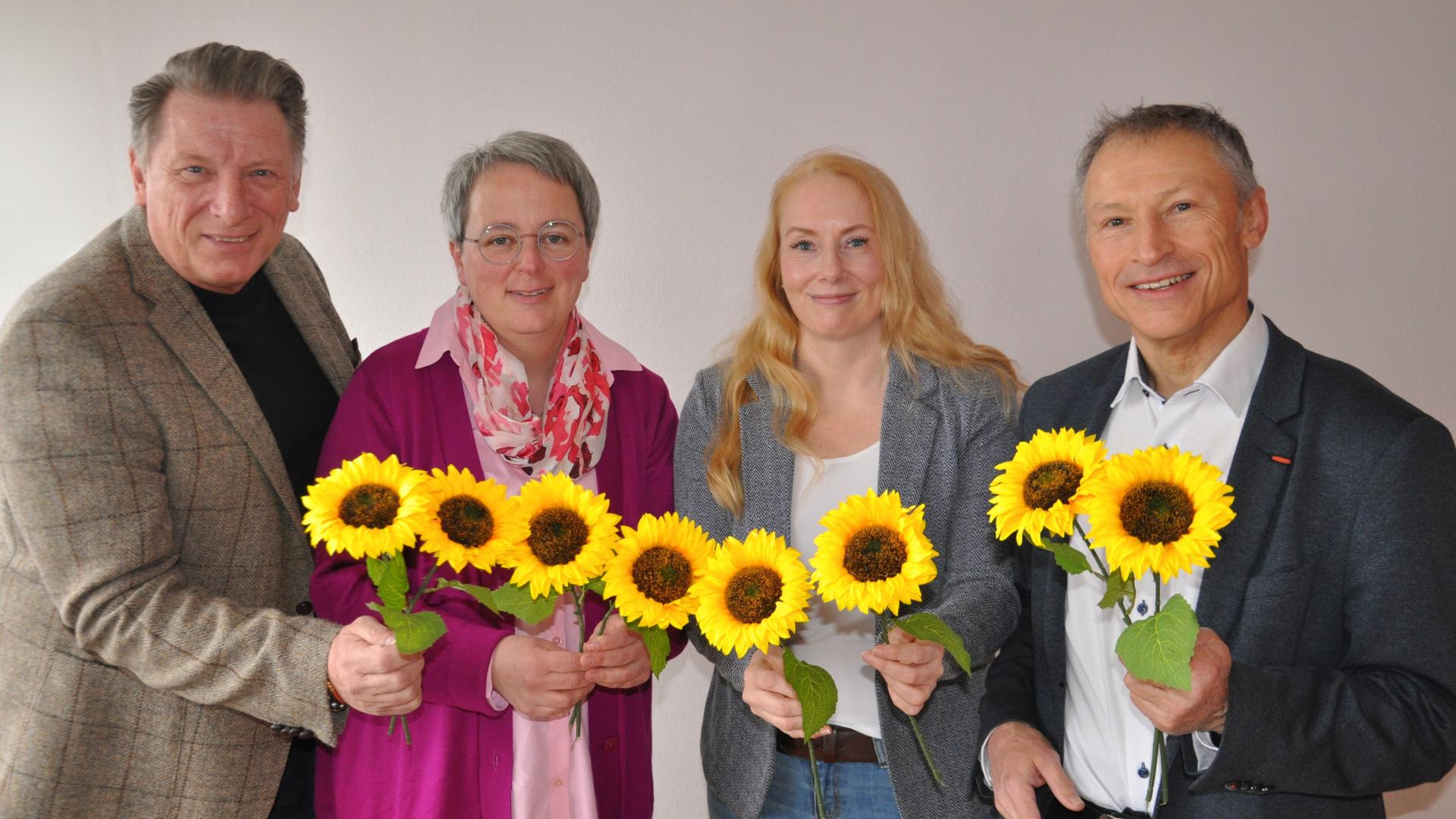 Zwei Männer und zwei Frauen halten Sonnenblumen in die Kamera