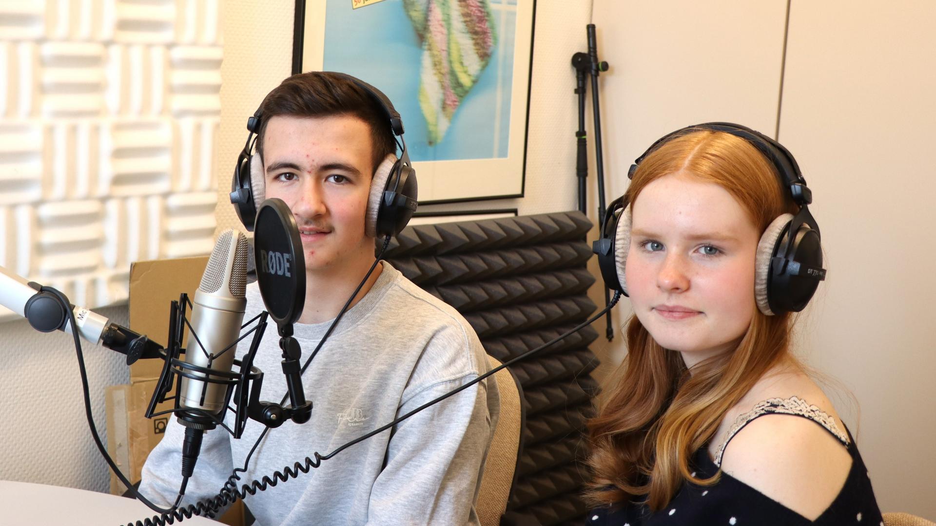 zwei Schüler sitzen mit Kopfhörern vor einem Mikrofon