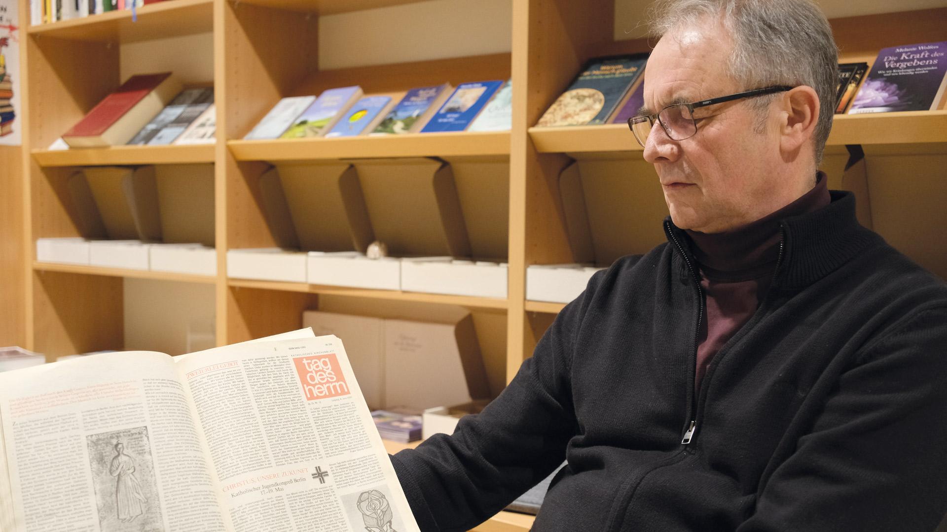 Peter Paul Straube sitzt im Ökumenischen Domladen Bautzen und blättert in einer alten Ausgabe des TAG DES HERRN