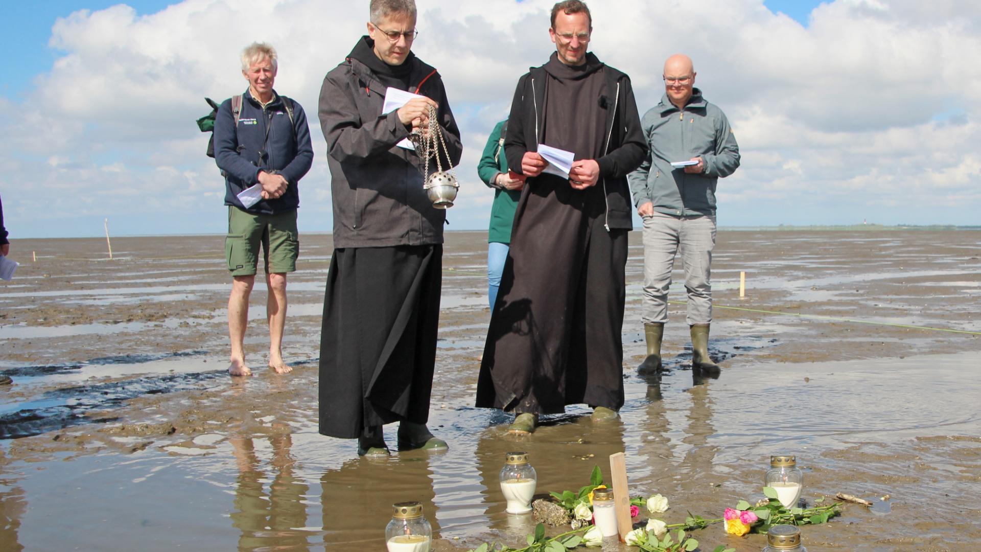 Menschen stehen im Watt und betrachten ein aus Rosen gelegtes Kreuz.