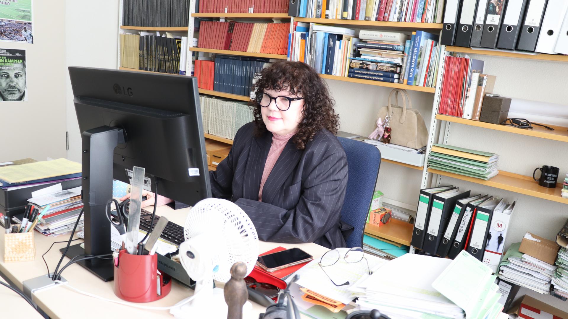 Eine Frau sitzt am Schreibtisch und schaut auf einen Bildschirm
