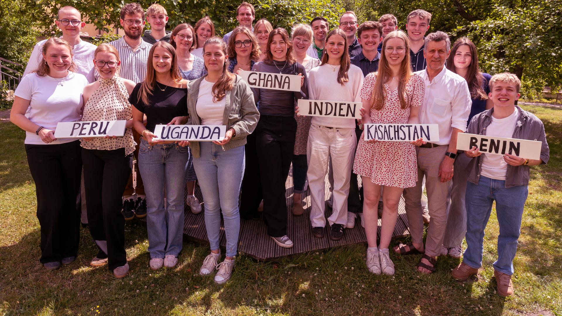 Ein Gruppenfoto mit etwa 20 jungen Menschen. Viele halten ein Schild in den Händen, auf dem der Name eines Landes geschrieben ist
