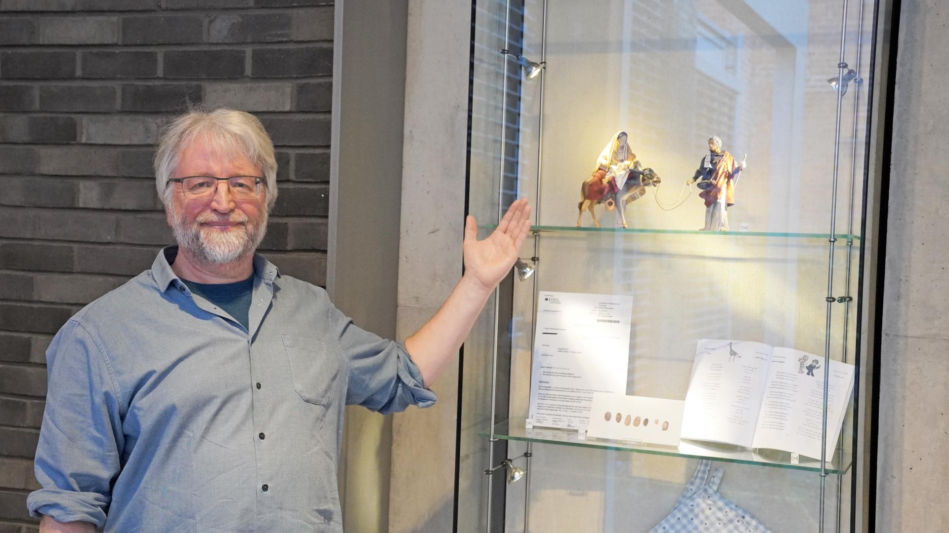 Ein Mann zeigt auf Figuren in einer Vitrine.