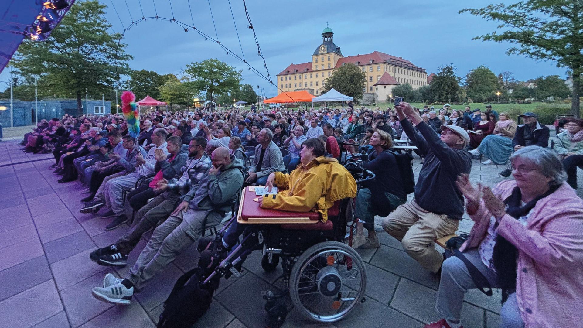 ein Publikum, in dem Menschen mit und ohne Behinderung sitzen, applaudiert